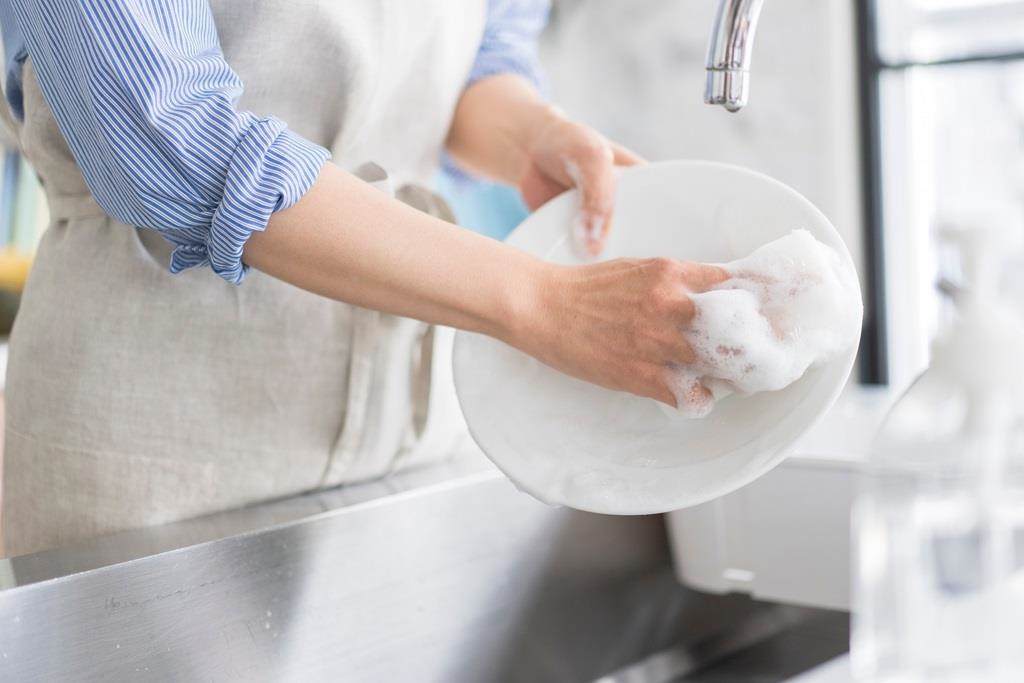 A little girl stood on a chair washing up crockery in a sink