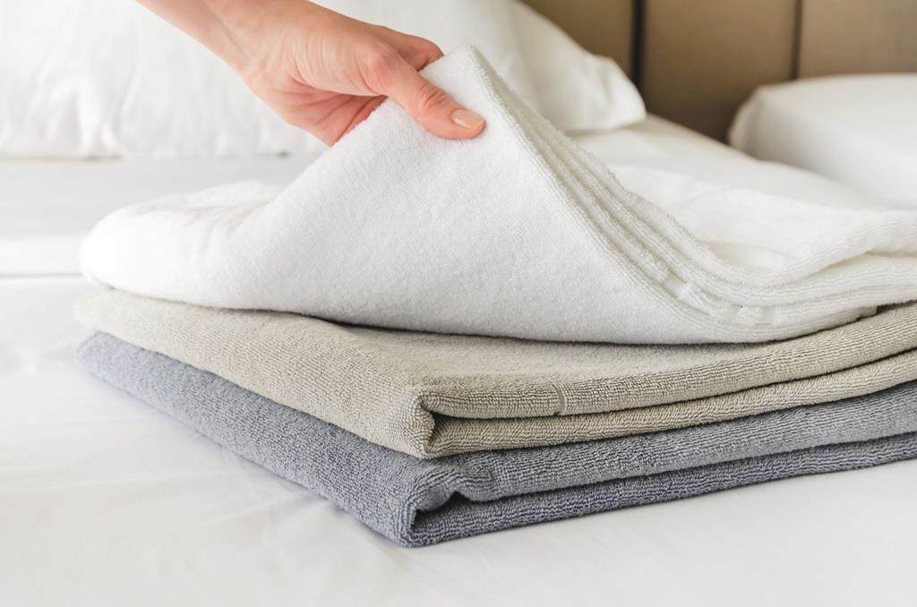 Hotel maid placing white towels on a clean bed